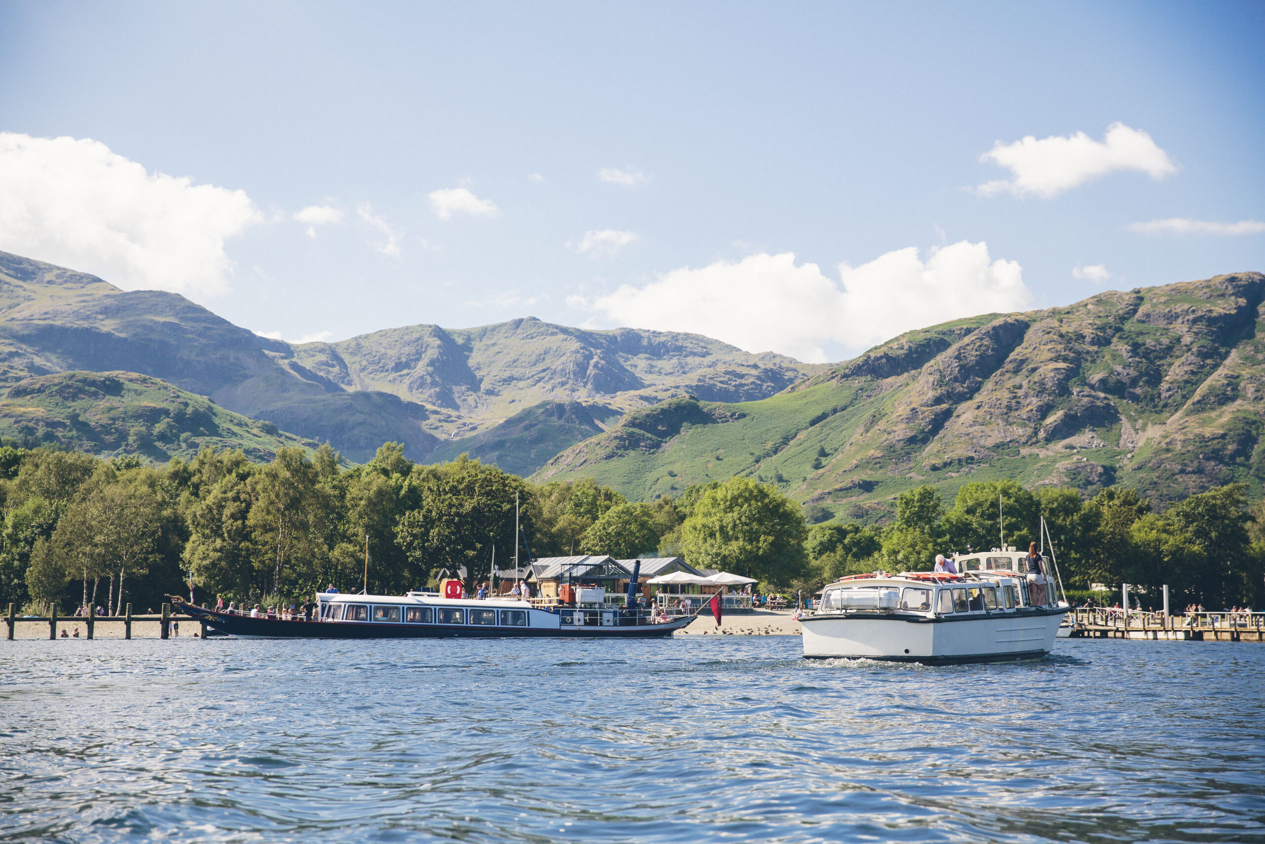 view of coniston boating centre, green woodland and fells from the lake