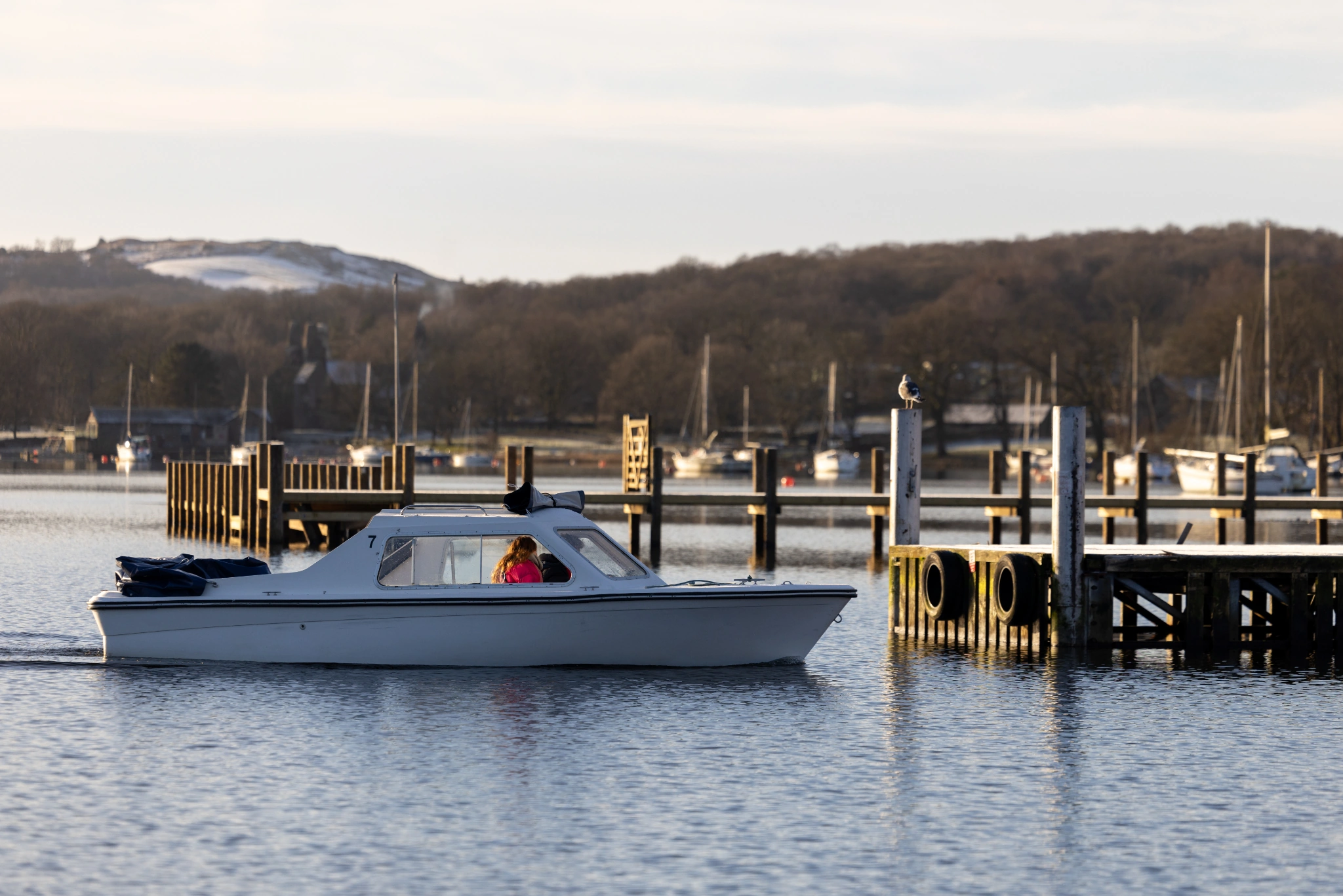 small white motor boat pulling into the wooden jetty on coniston water on a sunny, snowy winters day