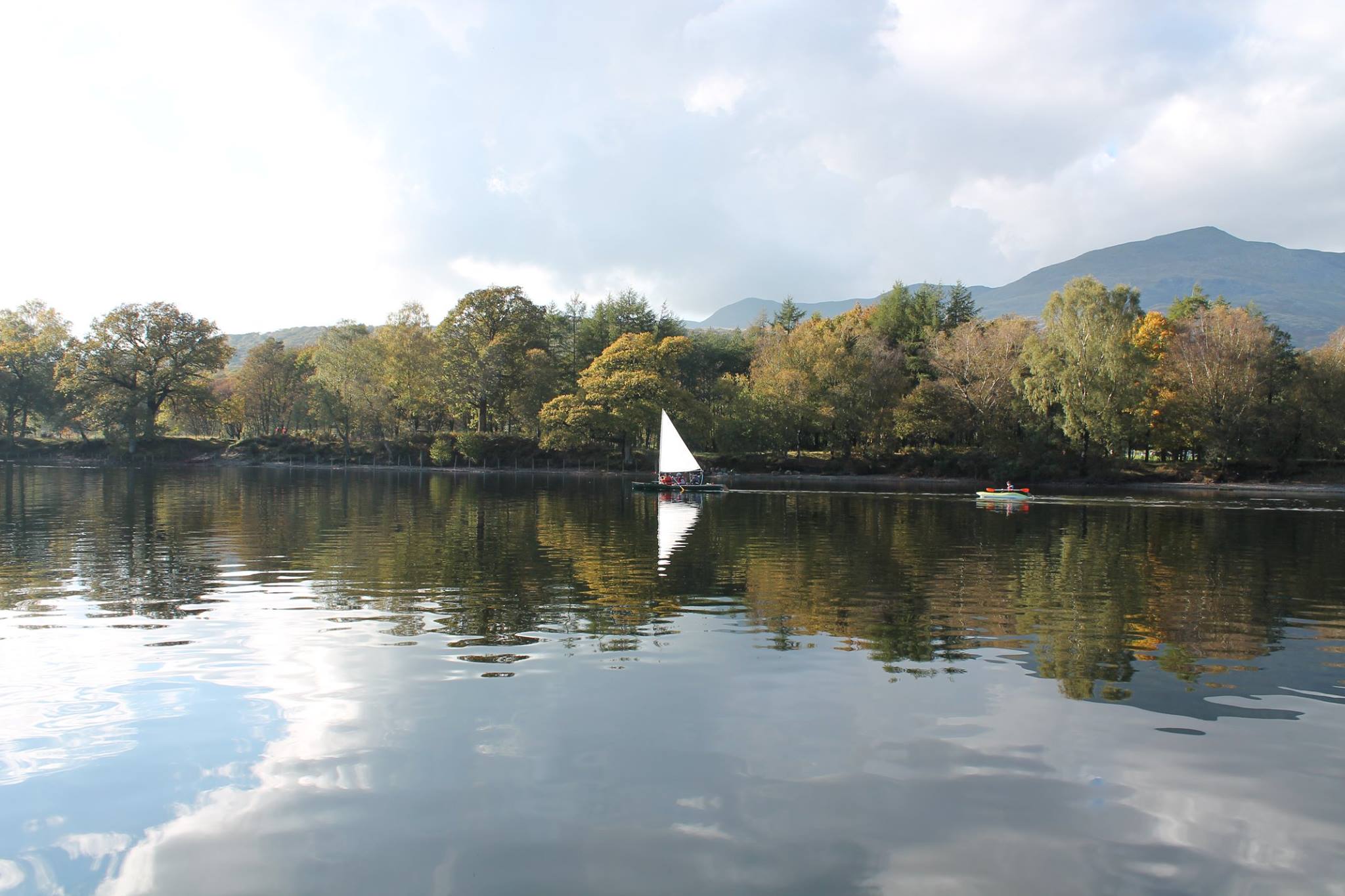 white sailing boat on a still coniston water with woodland behind
